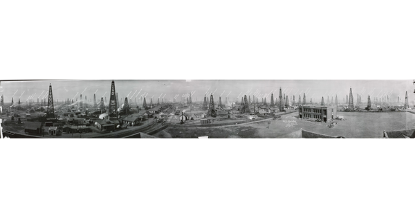 A black-and-white panoramic photograph of a massive oil field filled with wells and factory buildings.