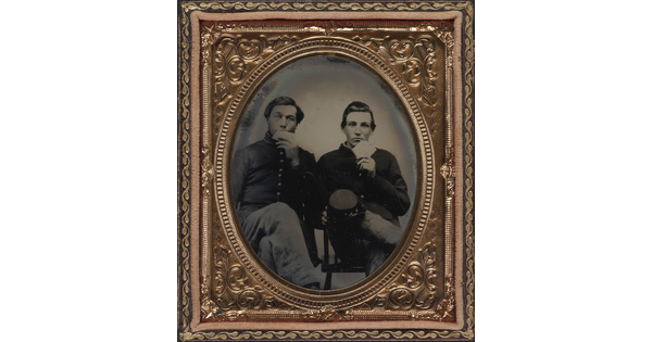 A black-and-white photograph in a decorative copper frame of two seated White men in military uniforms eating large crackers.