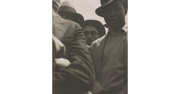 A black-and-white photograph of a close-up of a group of men wearing hats, sweaters, and jackets.