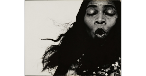 A black-and-white close-up photograph of a Black woman singing with her eyes closed.