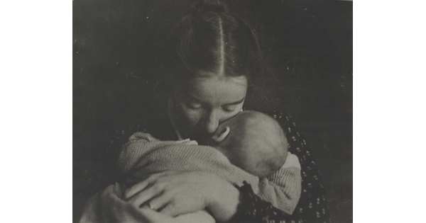 A black-and-white photograph of a White woman holding an infant to her chest while she rests her cheek on the infant's cheek.