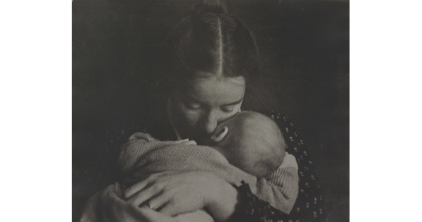 A black-and-white photograph of a White woman holding an infant to her chest while she rests her cheek on the infant's cheek.