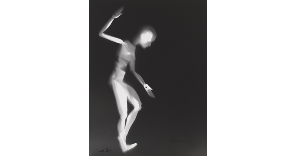 A black-and-white photograph of a white person-shaped puppet dancing on a black background.