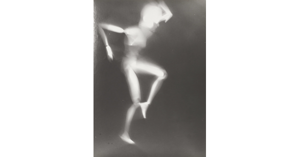 A black-and-white photograph of a white person-shaped puppet dancing on a black background.