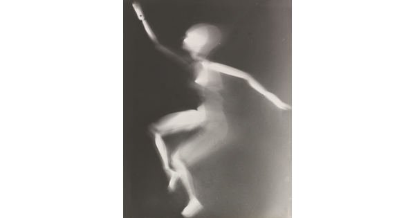 A black-and-white photograph of a white person-shaped puppet dancing on a black background.