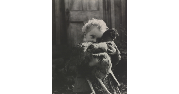 A black-and-white photograph of a White toddler holding a chicken close and obscuring part of her face.
