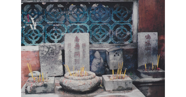 A color photograph of a shrine on a stone altar with incense sticks in stone holders of varying shapes.