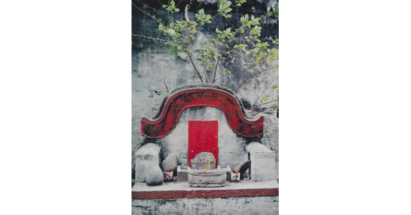 A color photograph of a stone altar with a red border above it and several incense sticks in various small vessels.