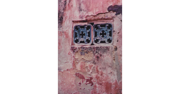 A color photograph of a red plaster wall containing two decorative window grates.