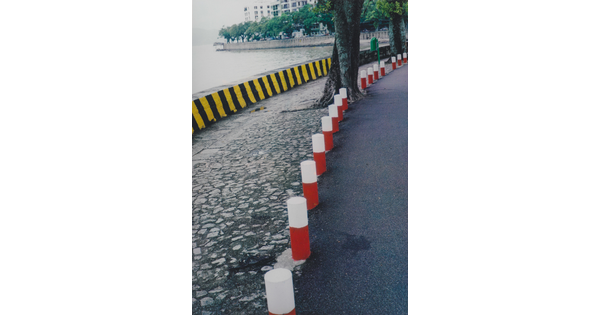 A color photograph of red and white bollards at the edge of a street, a stone sidewalk, and a yellow and black temporary floodwall.