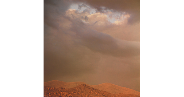 A color photograph of reddish mountaintops under dark, heavy clouds.