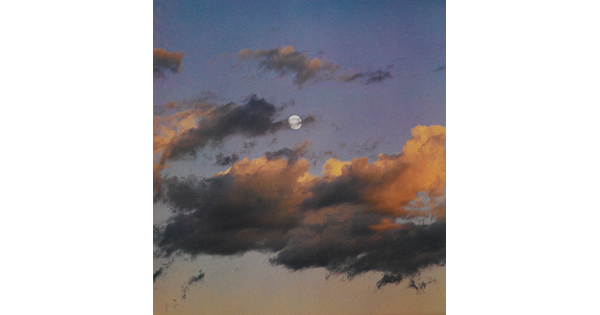 A color photograph of a full moon at dusk behind wispy, orange and dark clouds.