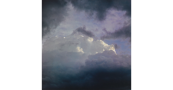 A color photograph of dark clouds framing brighter, fluffy clouds in the center.