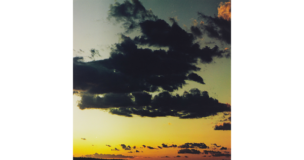A color photograph of dark clouds in a sky of orange, yellow, blue, and gray.