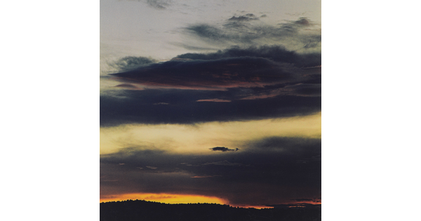 A color photograph of dark clouds in the sky and the sun setting at the horizon.