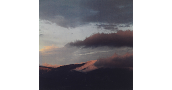 A color photograph of a mountain range with clouds in a blue and pink sky.