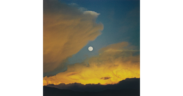 A color photograph of a full moon in a dark blue sky with yellow swirling clouds.