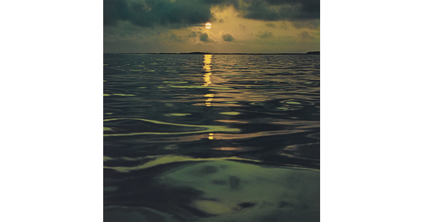 A color photograph of a sunset reflected over a calm, dark ocean.