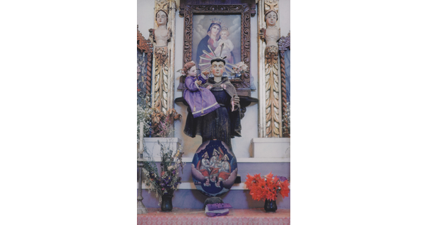 A color photograph of a decorative church altar with a statue of a saint holding a baby Christ figure in a purple robe.