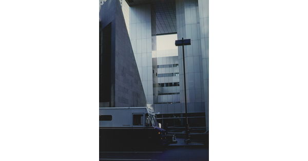 A color photograph of a delivery van parked in front of a modern skyscraper.