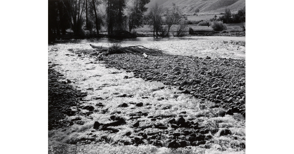 A black-and-white photograph of a mountain river bubbling through a gravel bar.