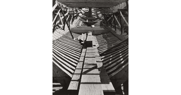 A black-and-white photograph of the inside wood frame of an unfinished ship.