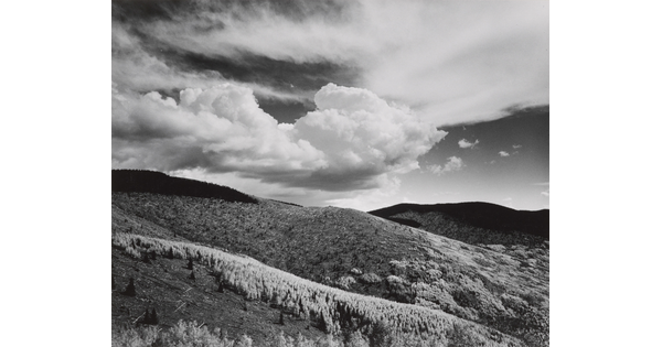 A black-and-white landscape photograph of a mountainous terrain under a partly cloudy sky.