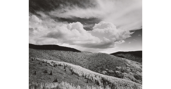 A black-and-white landscape photograph of a mountainous terrain under a partly cloudy sky.