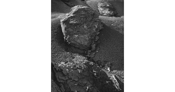 A black-and-white photograph of highly-textured, flaky rocks on a sandy slope.