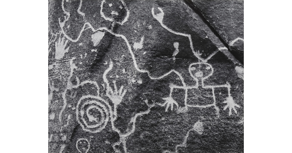 A close-up black-and-white photograph of symbols, several showing human forms, carved on a rock.