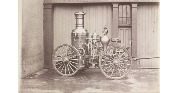 A black-and-white photograph of a parked wagon with a large tank and other mechanical features.
