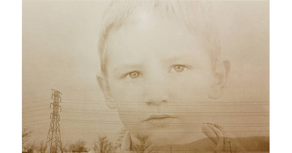A sepia-toned double-exposed photograph of the face of a young White child over a landscape of powerlines and hills.