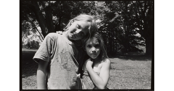 A black-and-white photograph of two young White girls, the taller one resting her head on the head of the other.