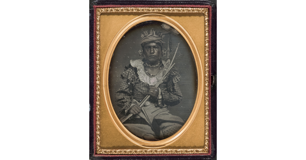 A framed black-and-white photograph of an Indigenous person holding a bow and arrow across their chest.