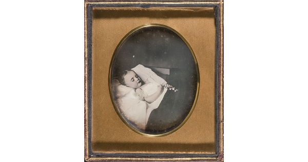 A black-and-white photograph in a gold frame of a child with closed eyes laying in bed with a toy in her clasped hands.