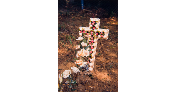 A color photograph of a small cross made of egg cartons and flowers on a freshly dug grave.