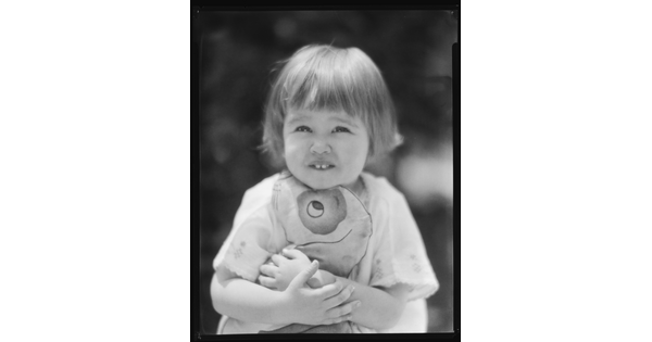 A black-and-white image of a young White child with short hair hugging a stuffed toy.