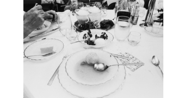 A black-and-white photograph of a place setting of a bowl of soup surrounded by dishes, glasses, and silverware.
