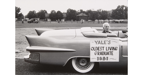 A black-and-white photograph of an elderly White man seated in the back of a convertible; a sign on the car reads, "Yale's oldest living graduate, 1881."