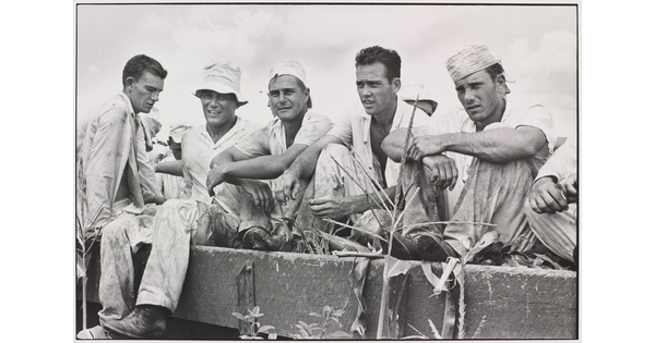 A black-and-white photograph of five young White men in dirty work clothes sitting in a wagon.