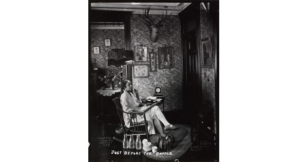 A black-and-white photograph of a Black woman in a rocking chair, holding a rolling pin on her lap, waiting at a front door.
