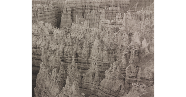A black-and-white landscape photograph of banded rock formations in a canyon.