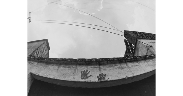 A black-and-white photograph looking up at a concrete lintel that has two distinct handprints on it.
