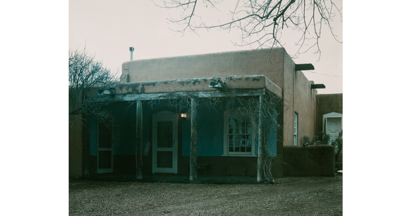 A color photograph of an adobe building with a wooden porch.