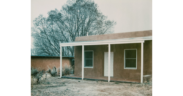 A color photograph of an adobe building with a wooden porch.