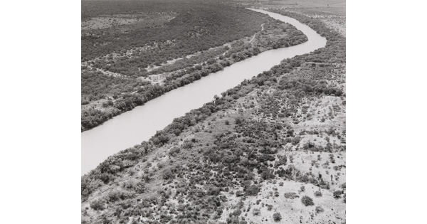 A black-and-white aerial photograph of a river running through a scrubby landscape.