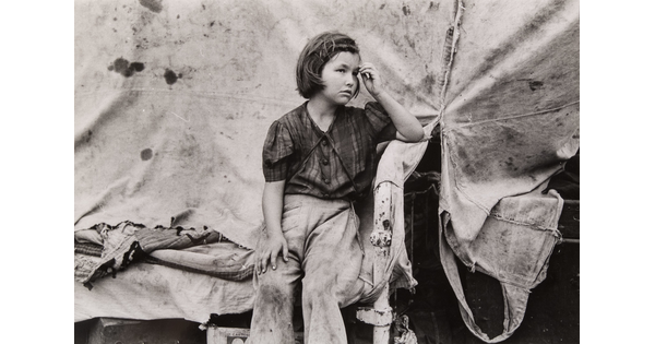 A black-and-white photograph of a young White girl wearing dirty clothes, one hand held up to her forehead, sitting in front of a canvas tent.