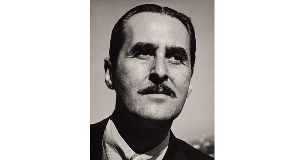 A black-and-white photograph of a White man with slicked back dark hair and a mustache.
