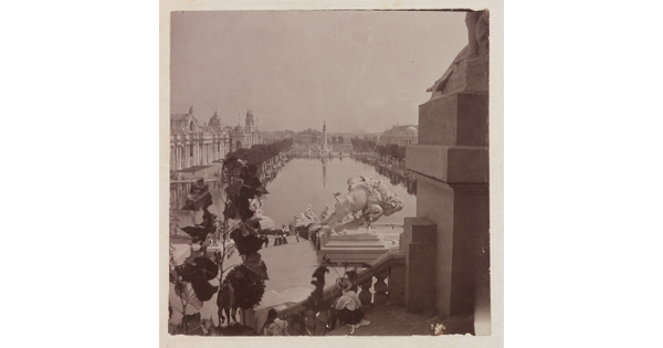 A black-and-white photograph of a tree-lined reflecting pool taken from the steps of a building showing other buildings and several sculptures, including a bison, lining the pool.