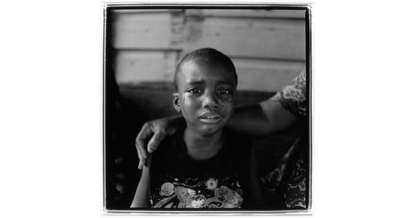A black-and-white photograph of a young Black child with tears streaming down their face and someone's arm around their shoulders.